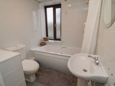 A bathroom with a toilet bathtub sink window and shower curtain at Providence Cottage in Ugglebarnby near Sleights