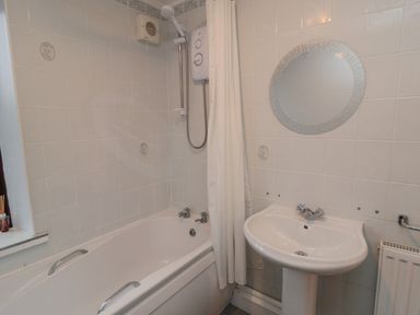 A bathroom with a bathtub shower sink and round mirror at Providence Cottage in Ugglebarnby near Sleights