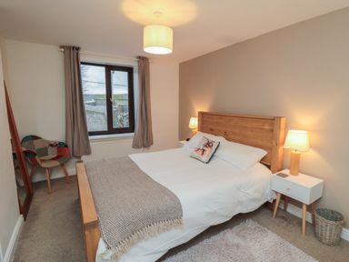 A bedroom with a wooden bed frame white bedding bedside tables with lamps a window and a patchwork chair at Providence Cottage in Ugglebarnby near Sleights