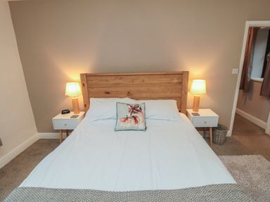 A bedroom with a wooden bed frame white bedding bedside tables with lamps at Providence Cottage in Ugglebarnby near Sleights