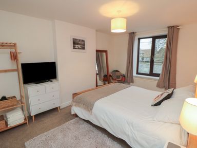 A bedroom with a bed a TV on a dresser a standing mirror and a window with curtains at Providence Cottage in Ugglebarnby near Sleights