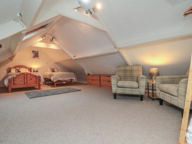 A bedroom with two single beds a rug two armchairs a side table with a lamp and wooden drawers at Providence Cottage in Ugglebarnby near Sleights