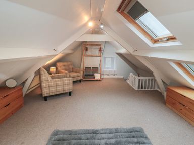 An attic room with two armchairs a wooden wardrobe two dressers skylights and a carpet at Providence Cottage in Ugglebarnby near Sleights