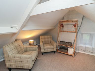 A small attic room with two armchairs a lamp on a side table and a wooden clothes rack with hangers and storage baskets at Providence Cottage Ugglebarnby near Sleights