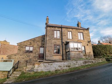 A stone house with multiple windows and chimneys on a sloped road at Providence Cottage in Ugglebarnby near Sleights