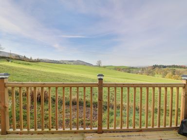 A wooden deck railing overlooking green fields and hills at Seren Lodge in Builth Wells