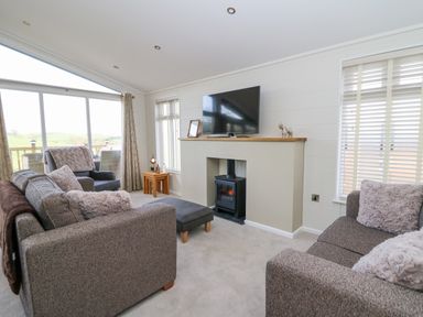 A living room with sofas a television on a mantle and large windows at Seren Lodge in Builth Wells