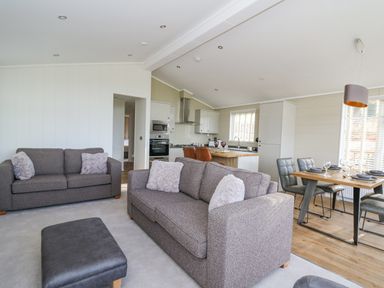A living room with two sofas, an ottoman, and an open kitchen and dining area at Seren Lodge in Builth Wells