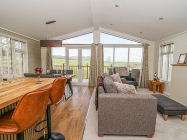 A living room with sofas and a dining table with chairs near large windows at Seren Lodge in Builth Wells