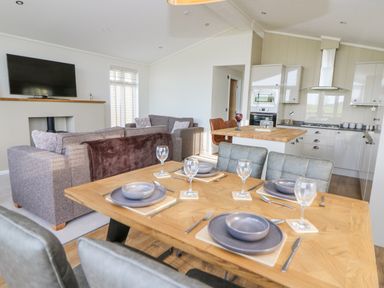 A dining table set with plates and glasses in a living room and kitchen area at Seren Lodge in Builth Wells