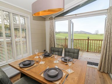 A dining table set for four with plates and glasses next to glass doors overlooking a green field at Seren Lodge in Builth Wells