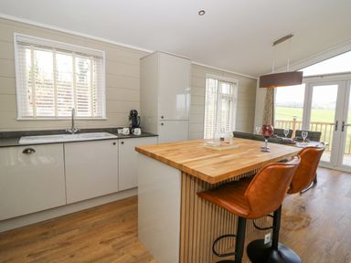 A kitchen with a wooden countertop island and brown bar stools next to a dining table with glassware at Seren Lodge in Builth Wells