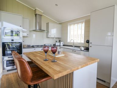 A kitchen with wooden island counter two stools window and appliances at Seren Lodge in Builth Wells