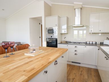 A kitchen with wooden countertop island three brown bar stools built in oven and microwave gas stove and white cabinets at Seren Lodge in Builth Wells