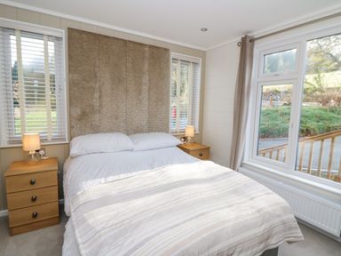 A bedroom with a double bed flanked by two wooden nightstands each with a lamp and large windows at Seren Lodge in Builth Wells