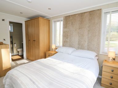 A bedroom with a double bed two bedside tables with lamps a wardrobe a chest of drawers and an open door to a bathroom at Seren Lodge in Builth Wells