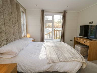 A bedroom with a bed beside a window a wooden desk with a television and a small lamp at Seren Lodge in Builth Wells