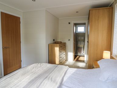 A bedroom with a bed a wooden dresser and wardrobe a door leading to a bathroom with a towel rack at Seren Lodge in Builth Wells