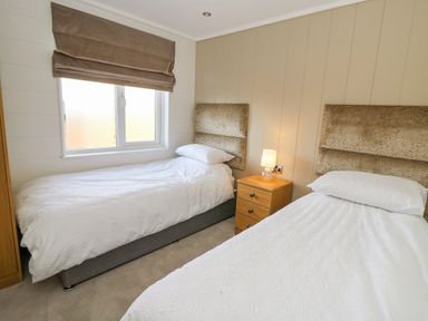 A bedroom with two single beds a nightstand with a lamp and a window with a brown blind at Seren Lodge in Builth Wells
