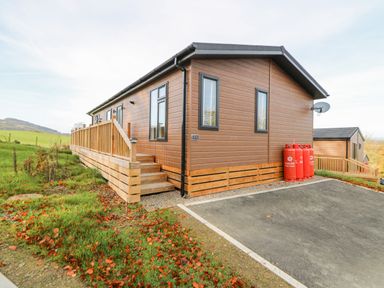 An exterior view of a wooden cabin with a fenced ramp and propane tanks on the side at Seren Lodge in Builth Wells
