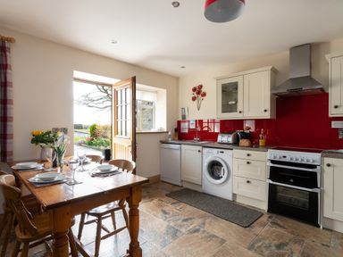 A kitchen with a wooden dining table set with plates and glasses an open door showing a garden at Teifi Cottage in Cardigan Near Cenarth