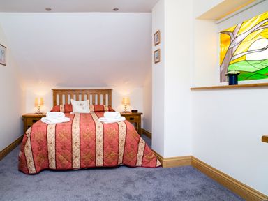 A bedroom with a double bed with red and beige striped bedding two bedside tables with lamps and a stained glass window at Teifi Cottage in Cardigan Near Cenarth