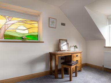 A wooden dressing table with a stool a small mirror and flowers next to a window with stained glass and another window in the corner at Teifi Cottage Cardigan Near Cenarth