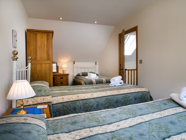 A bedroom with three single beds, wooden wardrobe, bedside table with lamp, dressing table, and an open door at Teifi Cottage Cardigan Near Cenarth