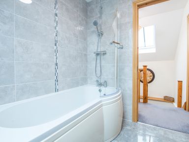 A bathroom with a bathtub shower combination and tiled walls at Teifi Cottage in Cardigan Near Cenarth
