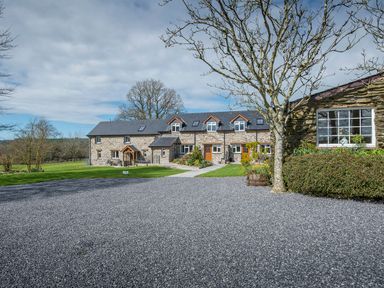 A gravel driveway in front of a stone building with dormer windows and a lawn with trees at Teifi Cottage in Cardigan Near Cenarth