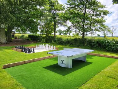 An outdoor area with a ping pong table and a large chess set on grass surrounded by trees at Teifi Cottage in Cardigan Near Cenarth