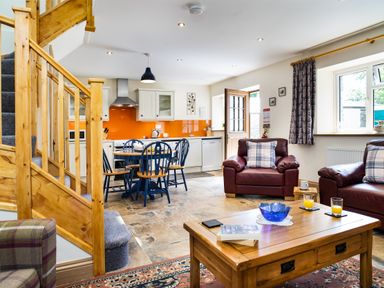 An open plan living area with kitchen dining table chairs leather armchairs and wooden staircase at Cych Cottage Cardigan Near Cenarth