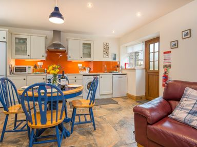 A kitchen with blue and wood dining chairs and table a red leather sofa and orange backsplash at Cych Cottage in Cardigan Near Cenarth