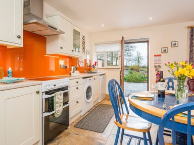 A kitchen with white cabinets orange backsplash and blue dining table with chairs and flowers at Cych Cottage Cardigan Near Cenarth