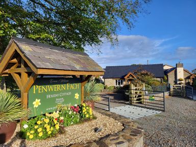 A holiday cottages sign with flowers and gravel driveway leading to stone cottages at Penwern Fach