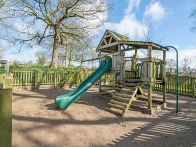 A wooden playground structure with a green slide and fenced area outdoors at Cych Cottage Cardigan Near Cenarth