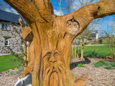 A wooden tree sculpture with carved faces of an old man, two owls, and a rabbit outdoors at Cych Cottage in Cardigan Near Cenarth