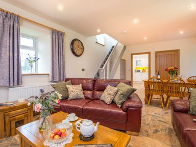 A living room with leather sofas a wooden coffee table with a teapot and flowers and a dining table with chairs at Towy Cottage Cardigan Near Cenarth