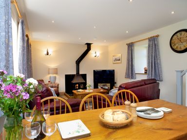 A living room with a fireplace red sofas a wooden table with bread a bottle of wine and glasses at Towy Cottage Cardigan Near Cenarth
