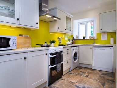A kitchen with white cabinets yellow backsplash a stove microwave washing machine and dishwasher at Towy Cottage in Cardigan Near Cenarth