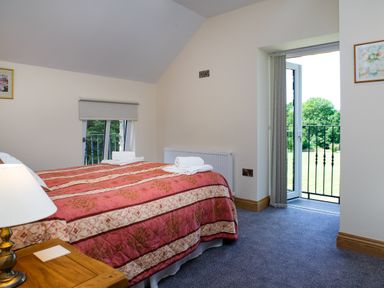 A bedroom with a bed covered in a patterned red and beige bedspread next to a window and an open door leading to a balcony at Towy Cottage in Cardigan Near Cenarth