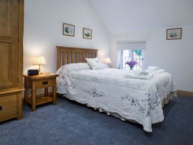 A bedroom with a wooden bed and nightstands with lamps and framed pictures on the wall at Towy Cottage in Cardigan Near Cenarth