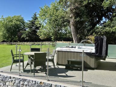 An outdoor patio with a round table and four chairs next to a hot tub with water jets at Towy Cottage Cardigan Near Cenarth