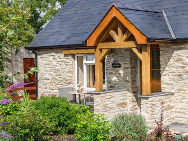 A stone cottage exterior with a wooden porch and garden furniture surrounded by plants and flowers at Gwaun Cottage Cardigan Near Cenarth