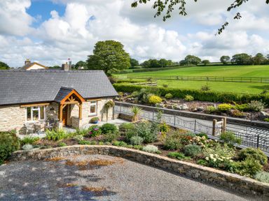 A stone cottage with a slate roof and garden in front of a green field at Gwaun Cottage Cardigan Near Cenarth