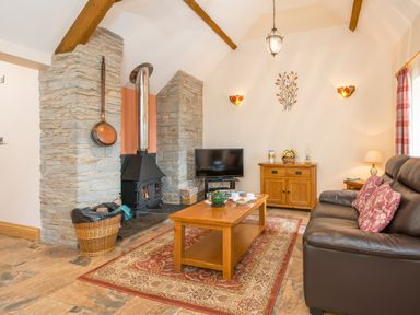 A living room with a wood stove television wooden furniture and a leather sofa at Gwaun Cottage Cardigan Near Cenarth