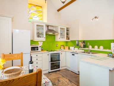 A kitchen with white cabinets green backsplash and wooden chairs at Gwaun Cottage Cardigan Near Cenarth
