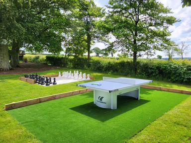 Outdoor area with a ping pong table and a large chess set on grass surrounded by trees at Gwaun Cottage in Cardigan Near Cenarth