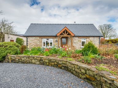 A stone cottage with a front garden of flowers and shrubs and a gravel driveway at Gwaun Cottage Cardigan Near Cenarth