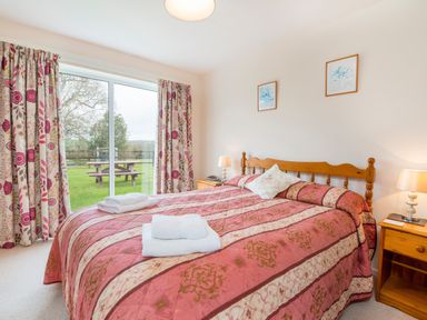 A bedroom with a double bed red patterned bedspread towels on bed bedside tables lamps and sliding glass door with floral curtains at Cothi Cottage in Cardigan Near Cenarth